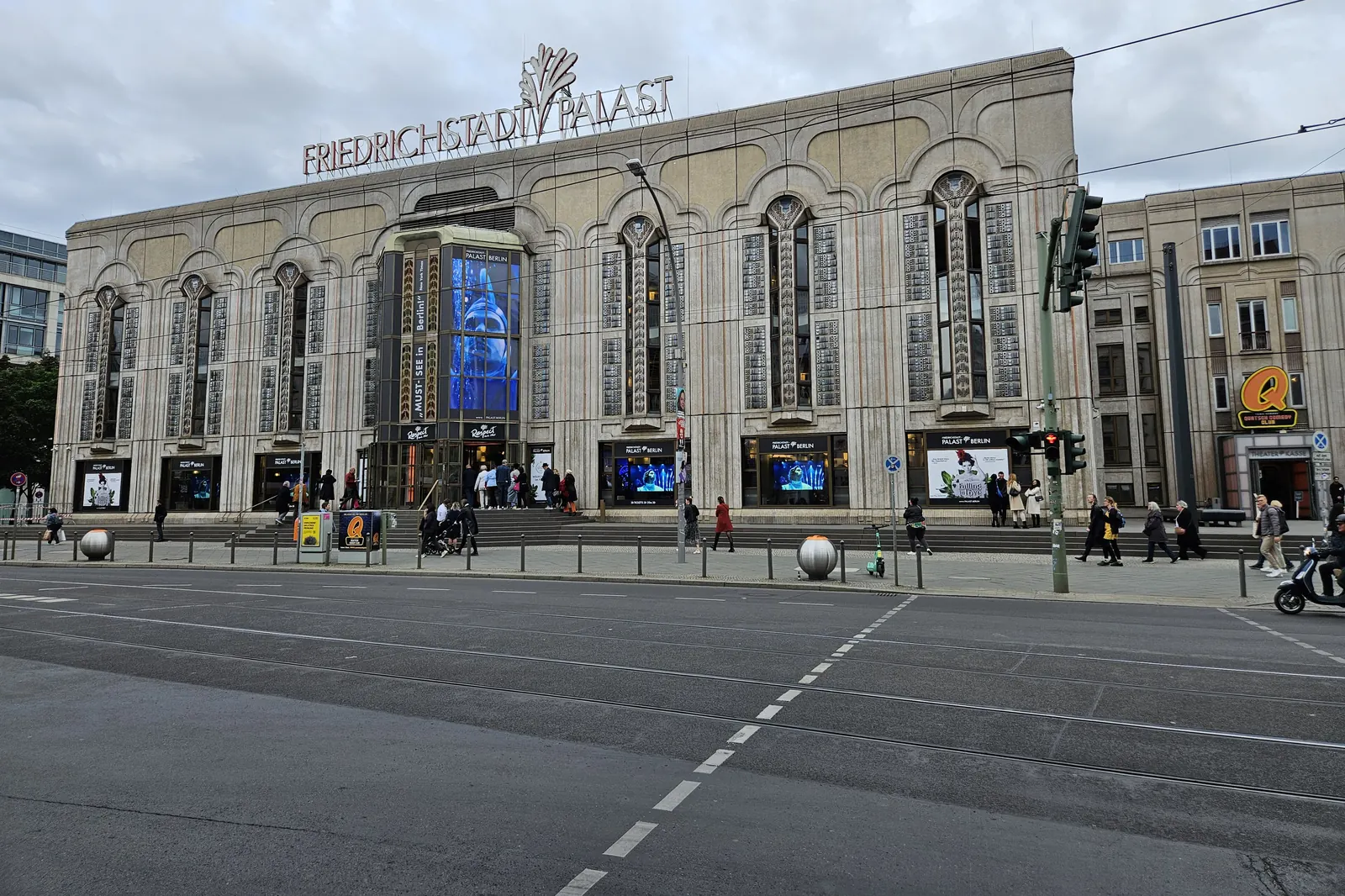 The stone front of the Friedrichstadt-Palast by day seen across the street, with its sign on the roof and tall arched windows